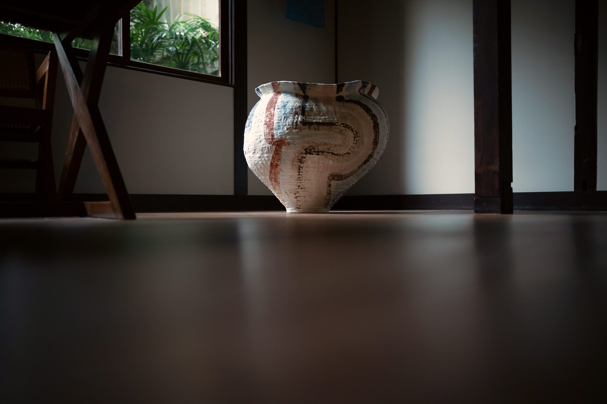 A large hand-built ceramic jar by Kazunori Hamana on a dark wooden floor, beside a window onto greenery.
