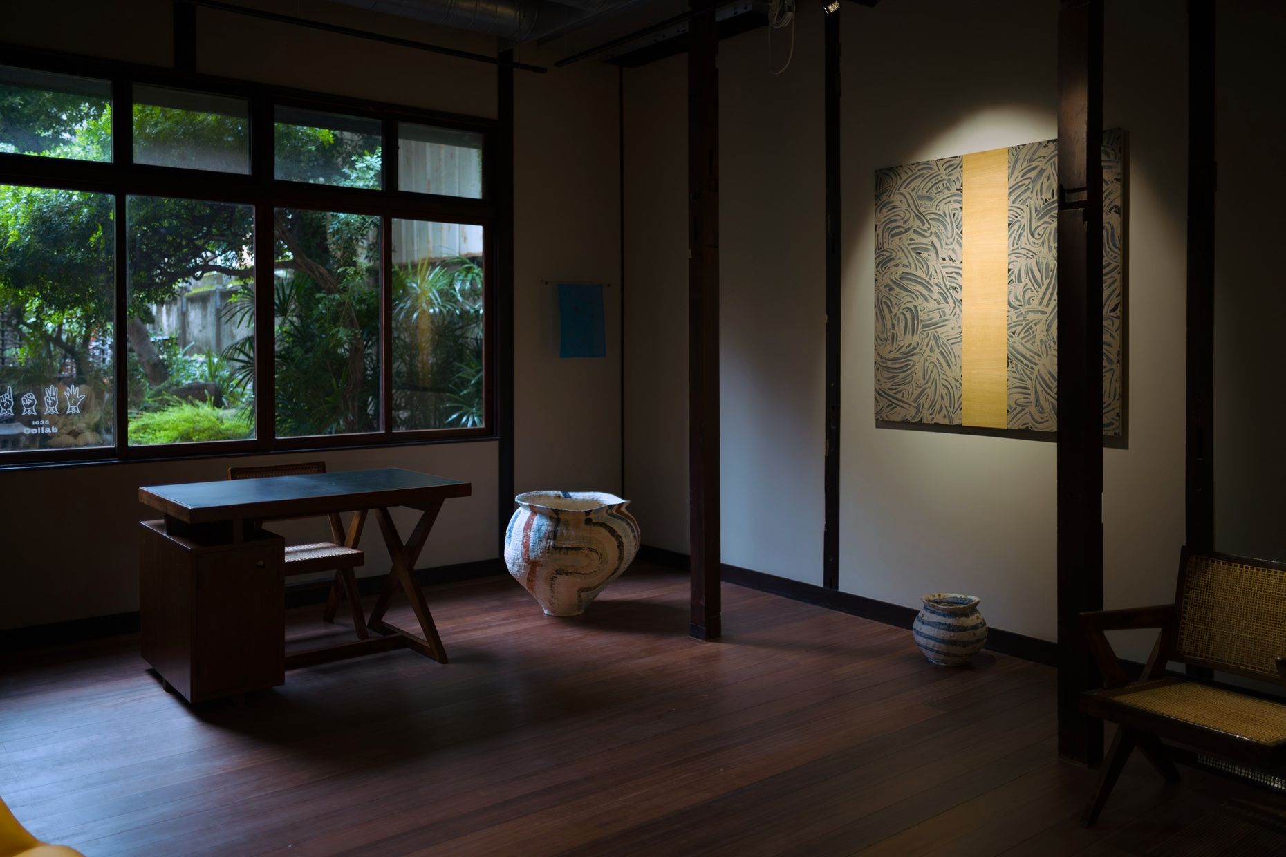 A room with windows onto a garden, a desk, ceramic jars on the floor and Richard Long's mud work on the wall.