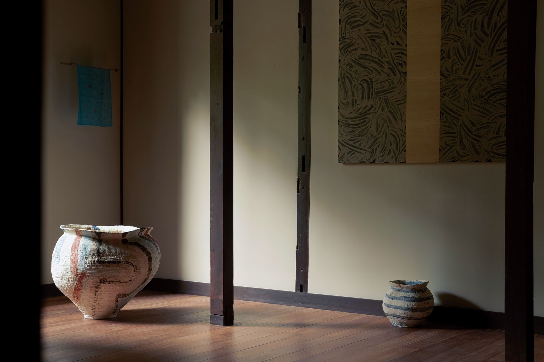 Two jars on a wooden floor along a pale wall, with a blue textile and Richard Long's work hanging above.