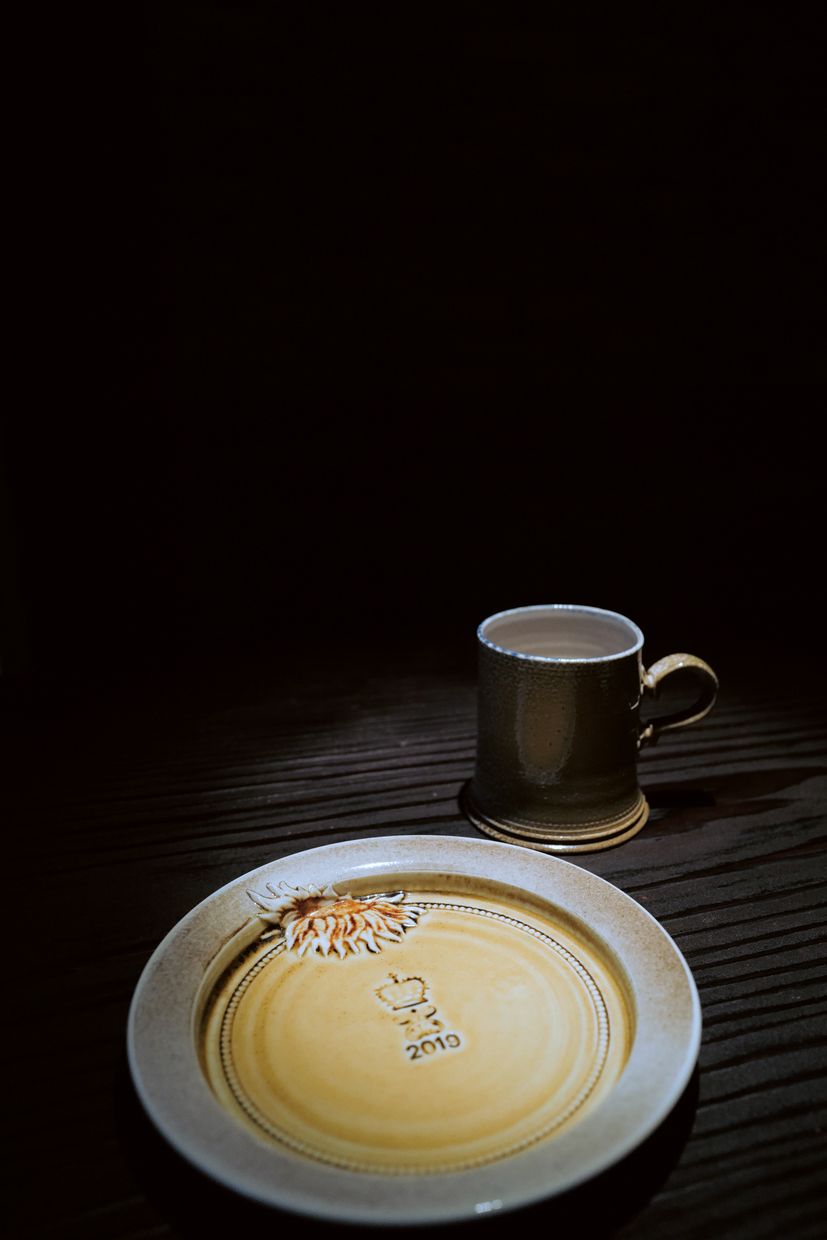A salt-glazed mug and a yellow-glazed plate stamped with a crown and the year 2010, lit on a dark table.