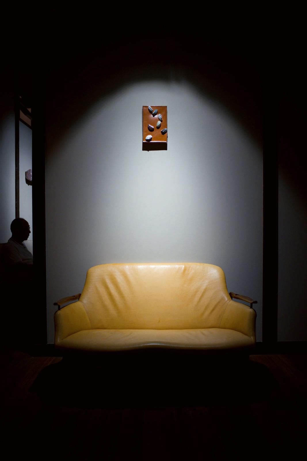 A small red ceramic panel lit on a wall above a yellow sofa.