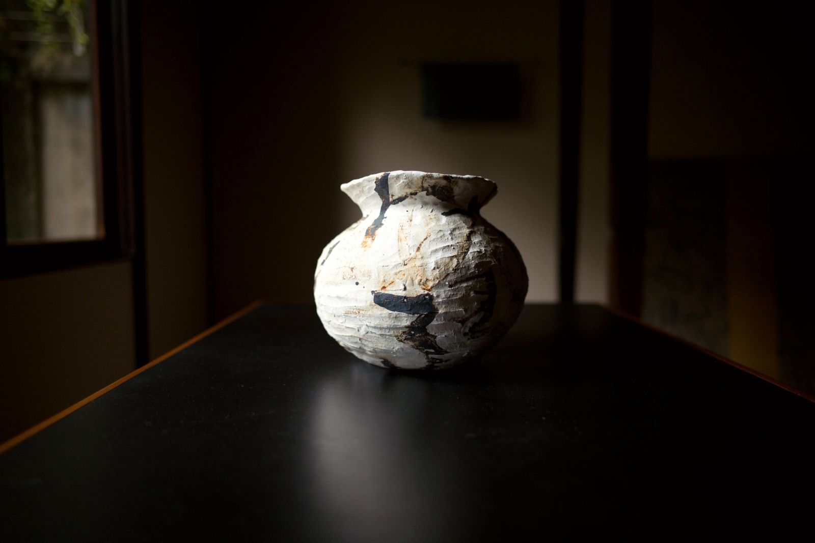 A white jar with brown and black marks on a black table in a dark room.