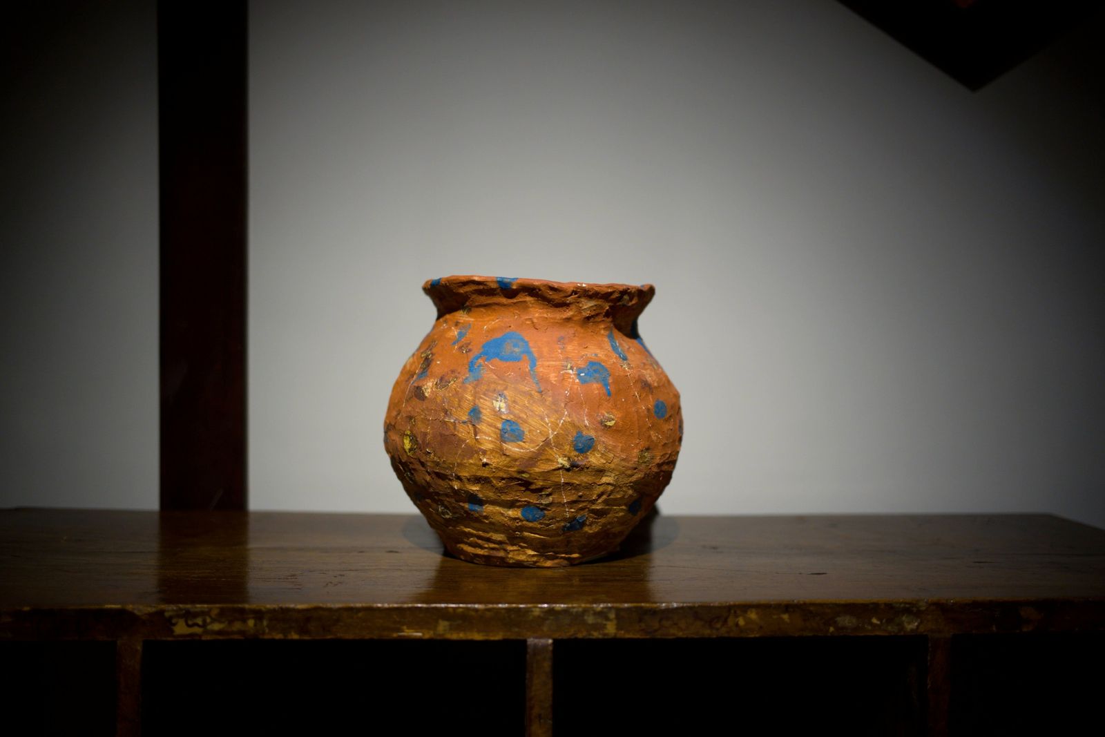An orange jar with blue dots on an old wooden table.