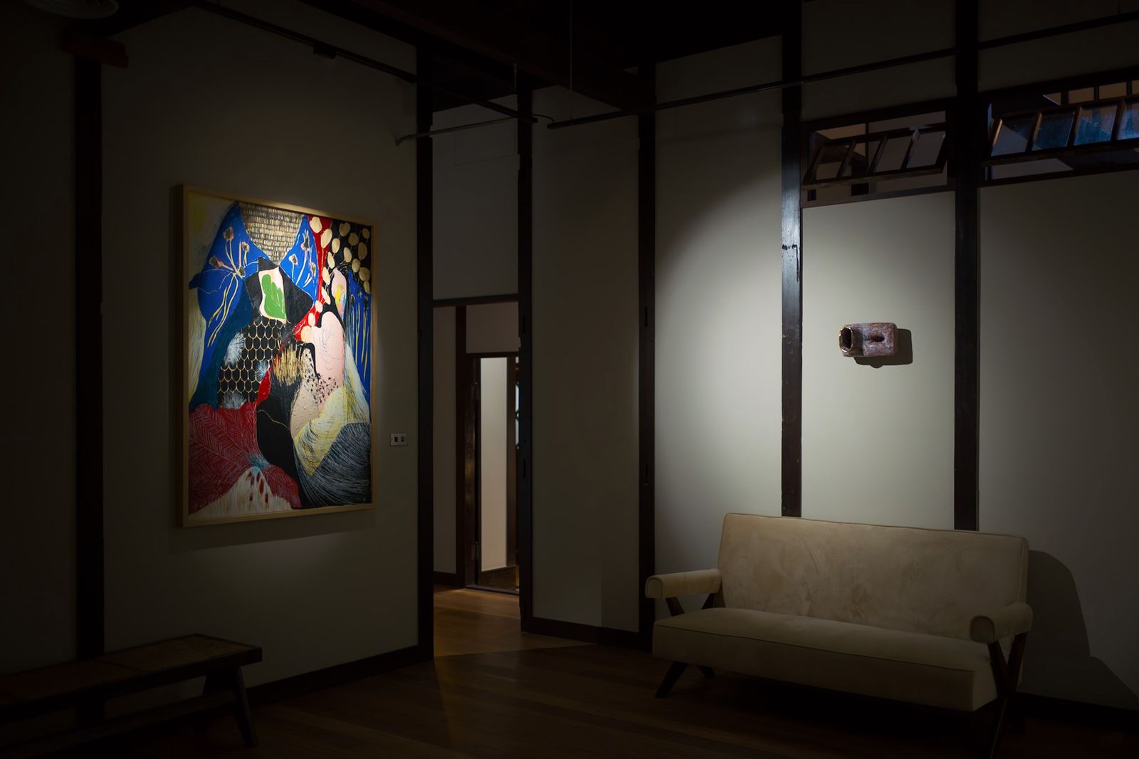 A large colourful painting on wood hanging in a room with a sofa.