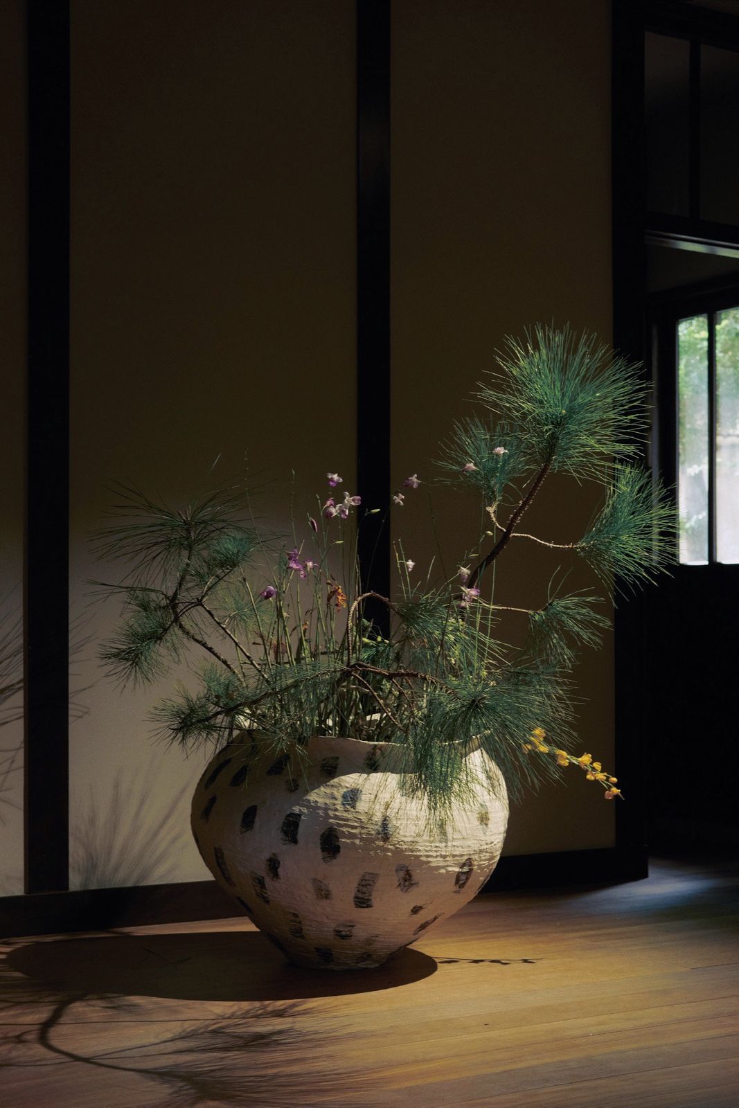 Pine branches and wildflowers arranged in a speckled jar on the floor.