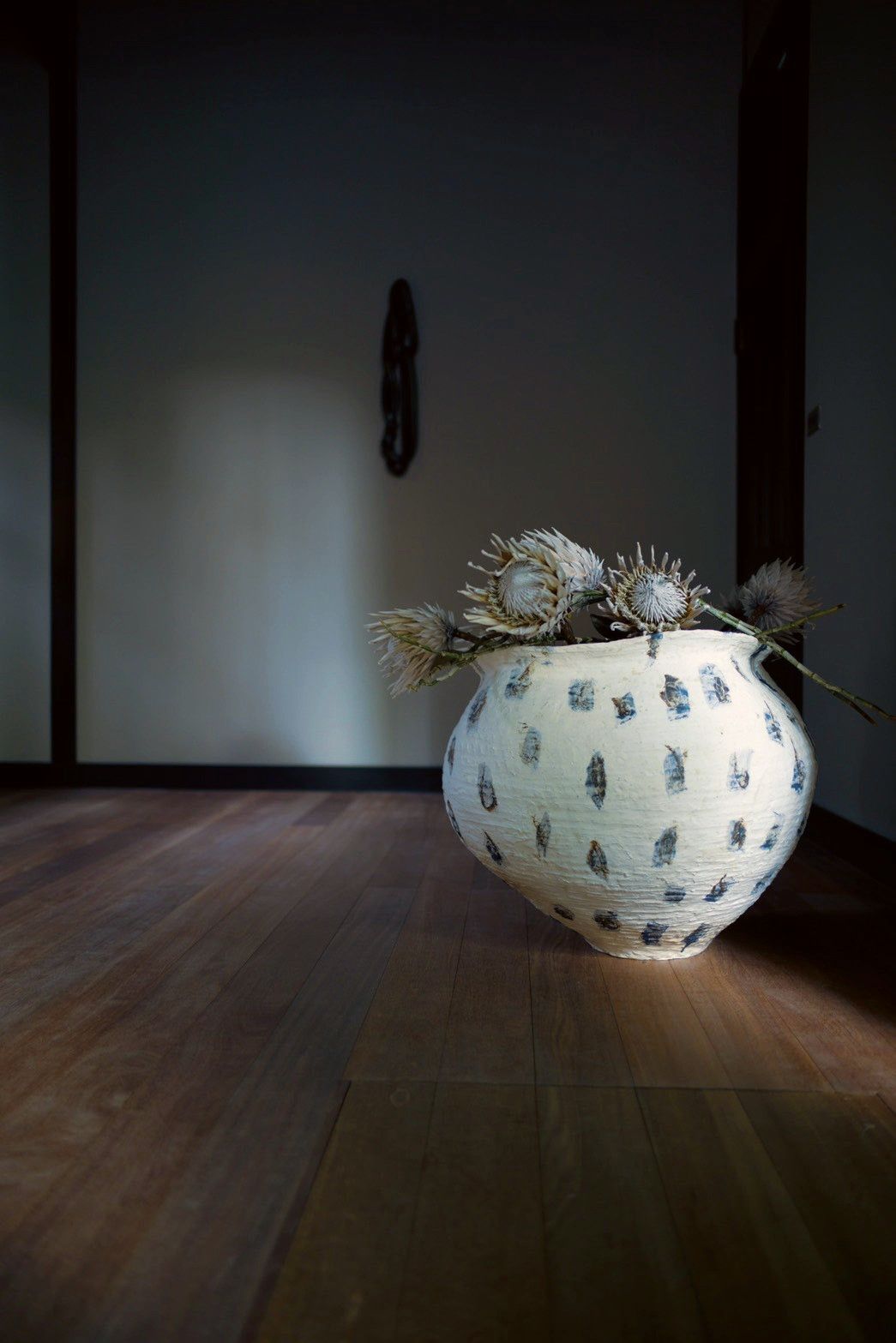 Dried protea flowers in the speckled jar on a wooden floor.