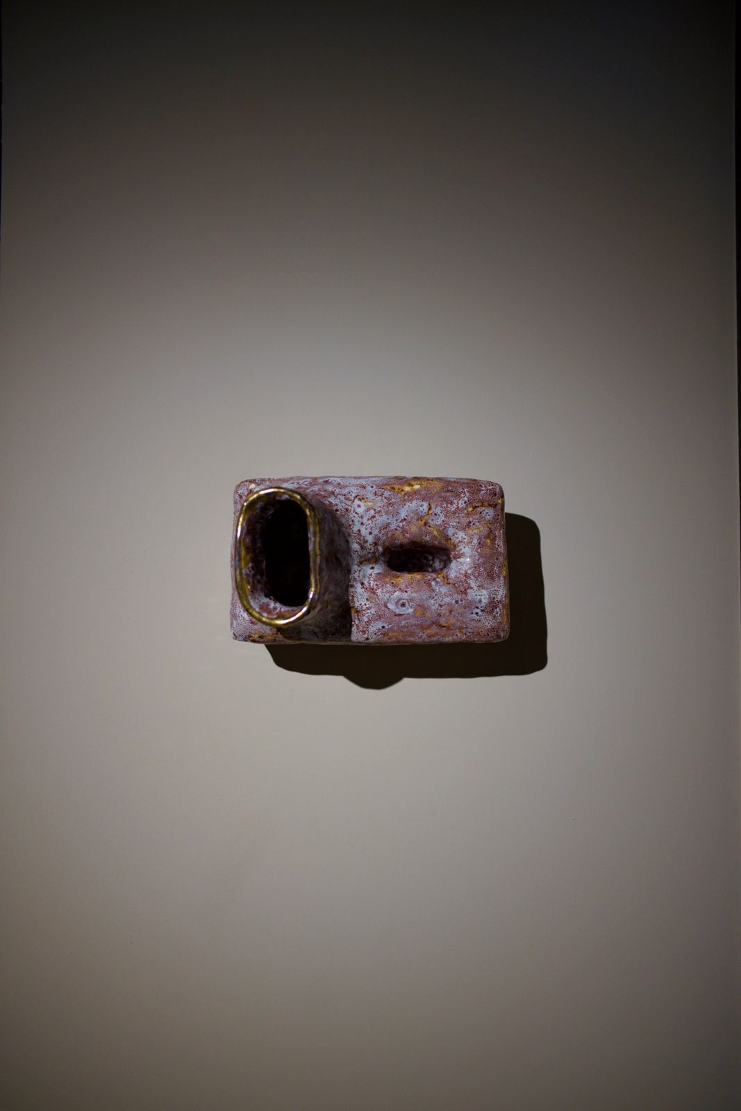 A small pink ceramic form with an oval opening, mounted on a wall in soft light.